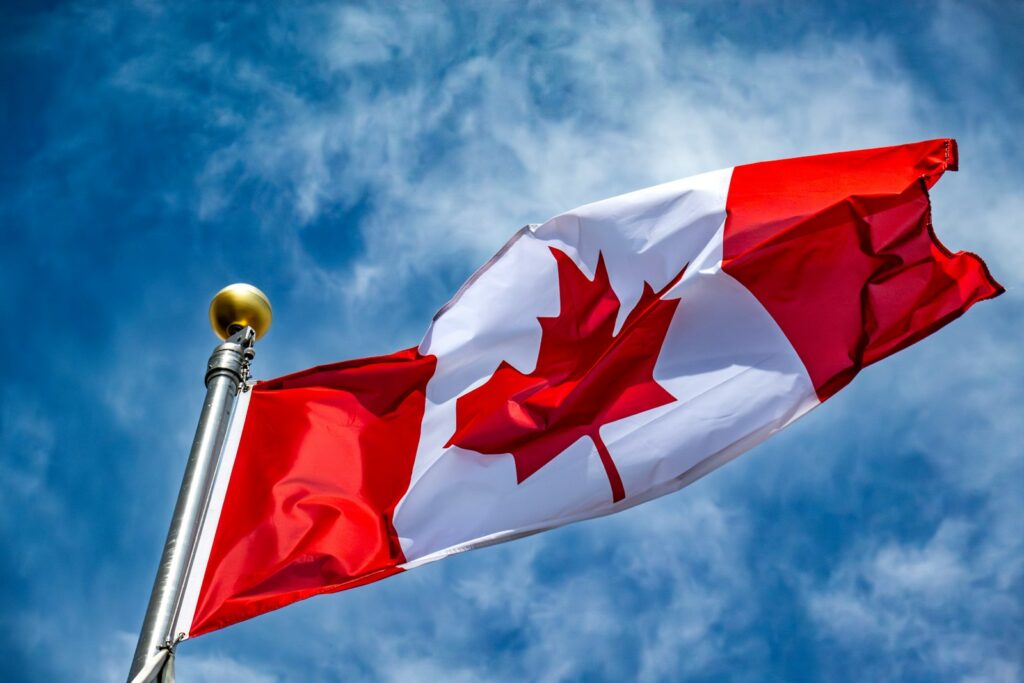 A Canadian flag waving on a flagpole against a blue sky with clouds