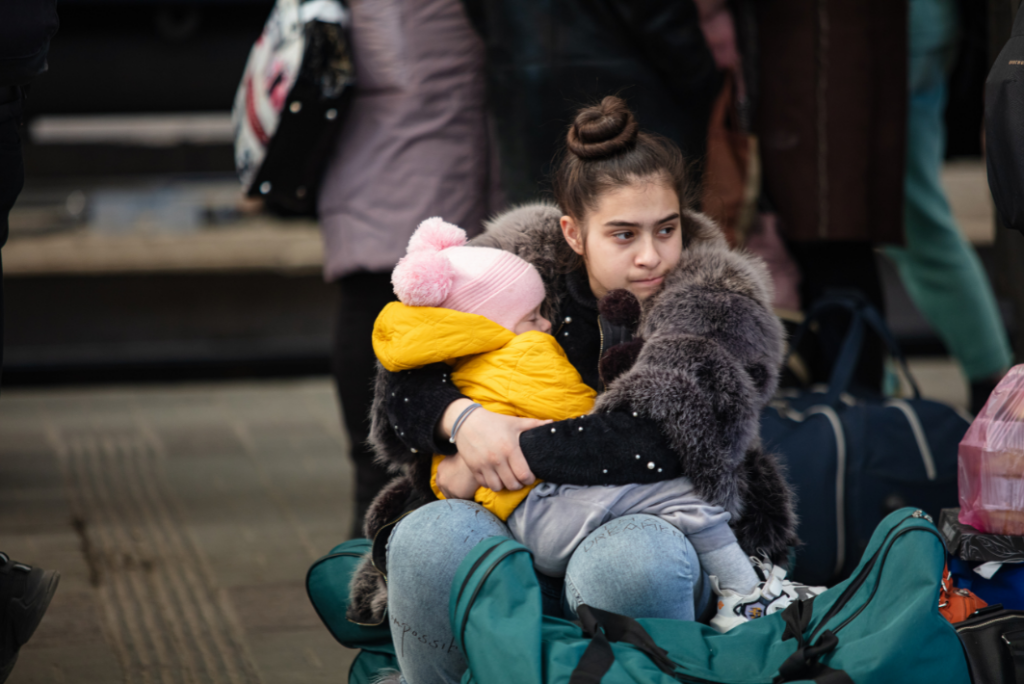 A child sitting on luggage holding a soft toy