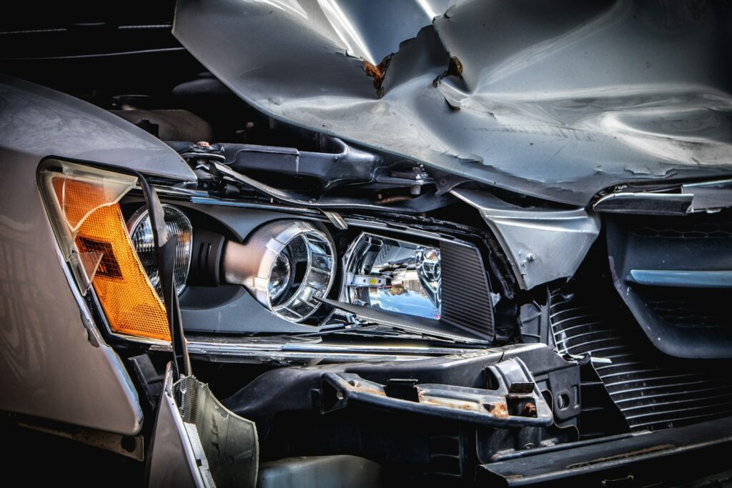 Close-up of a silver car with a crushed front end and broken headlight after a collision