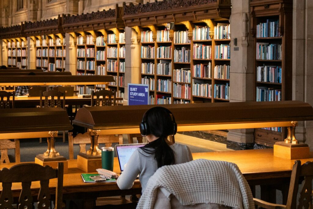International student studying at a library table with books and a laptop