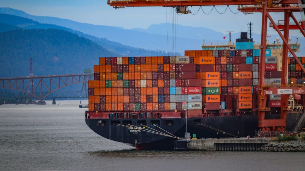 A container ship being loaded at the Port of Vancouver, with mountains in the background
